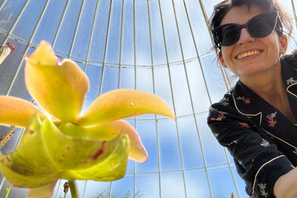Sam smiling beside a pitcher plant inside a glasshouse